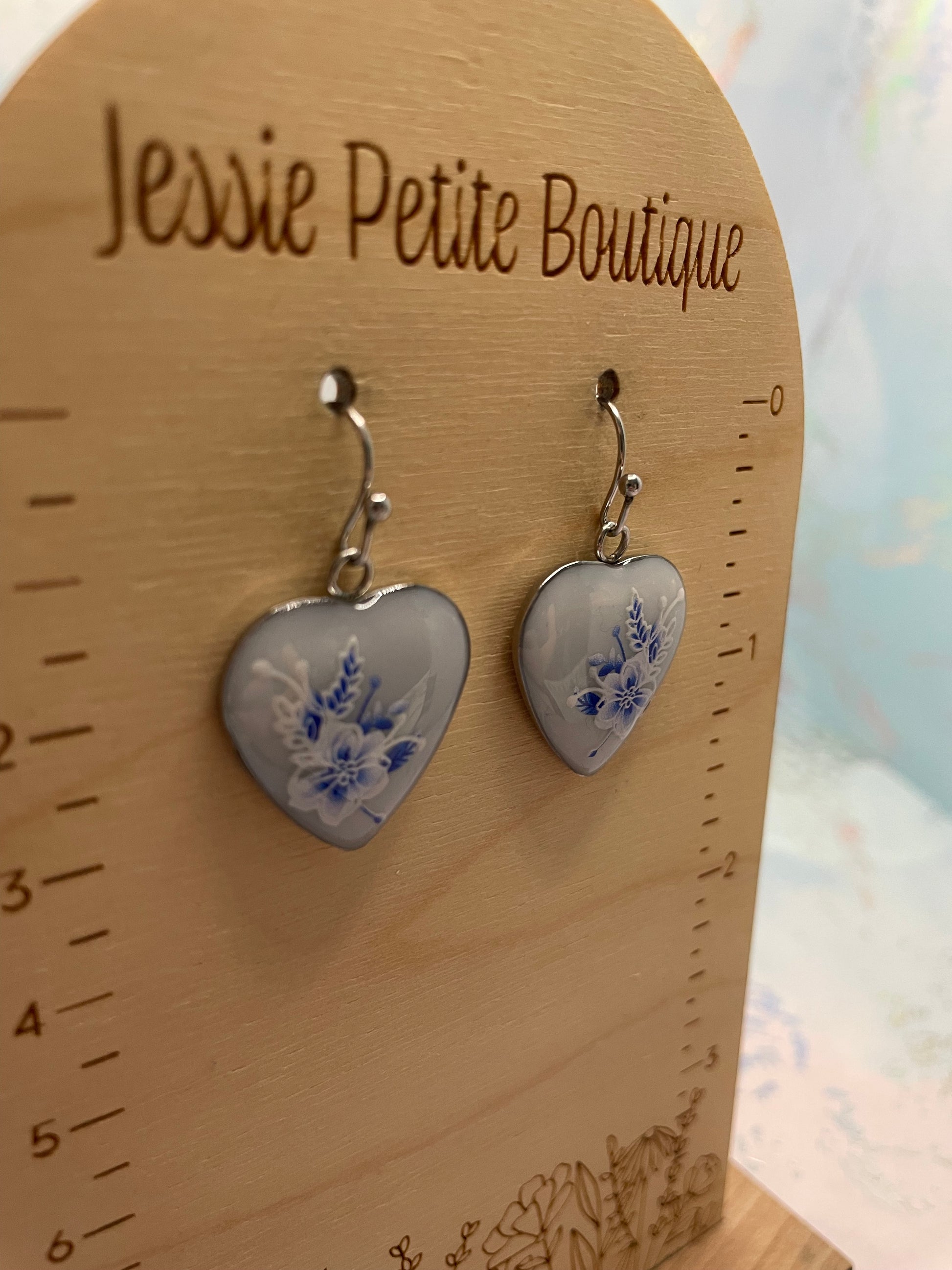Heart-shaped earrings with blue floral design on a wooden card with 'Jessie Petite Boutique' branding.
