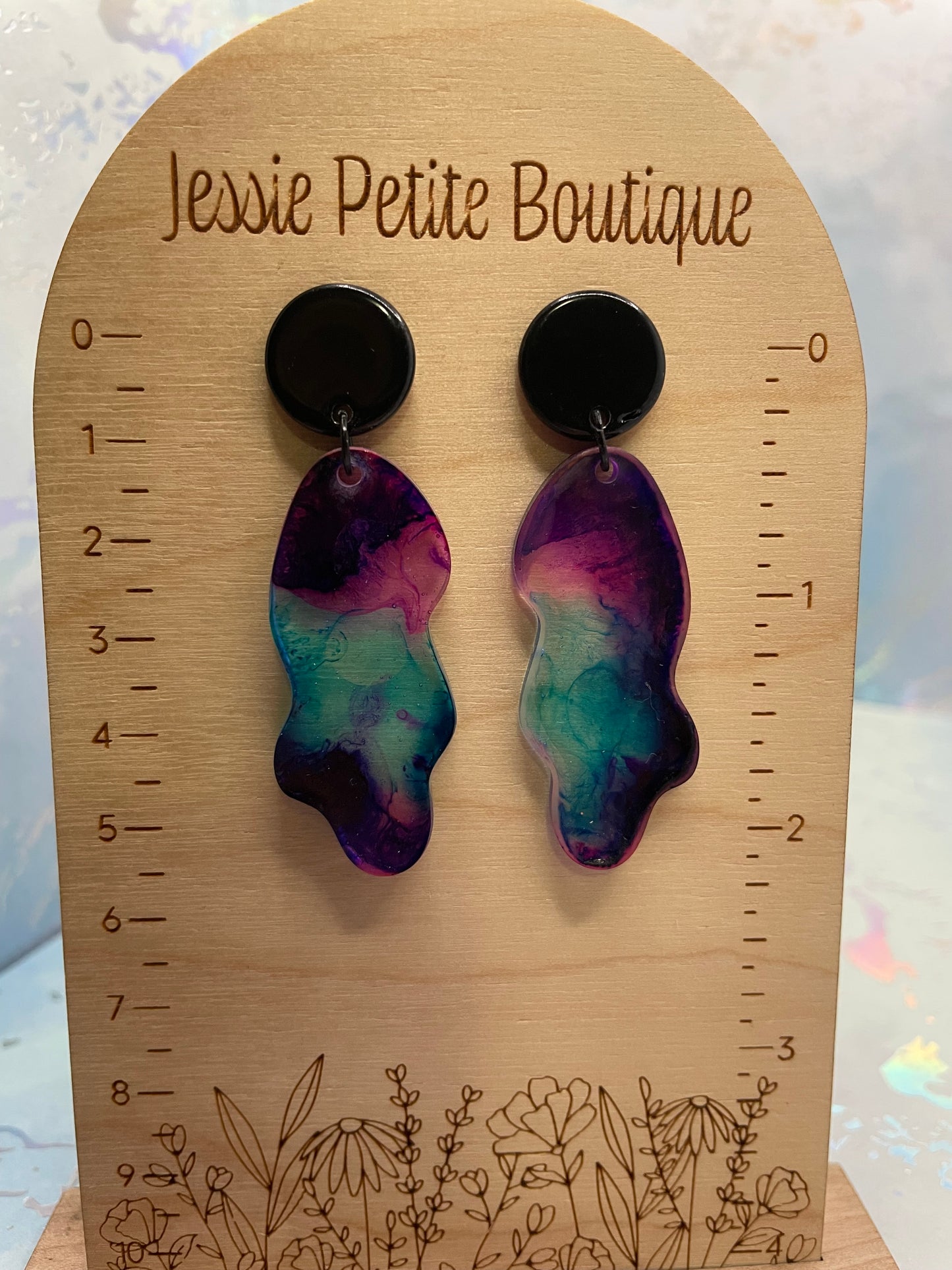 Colorful earrings on a wooden ruler with 'Jessie Petite Boutique' branding.