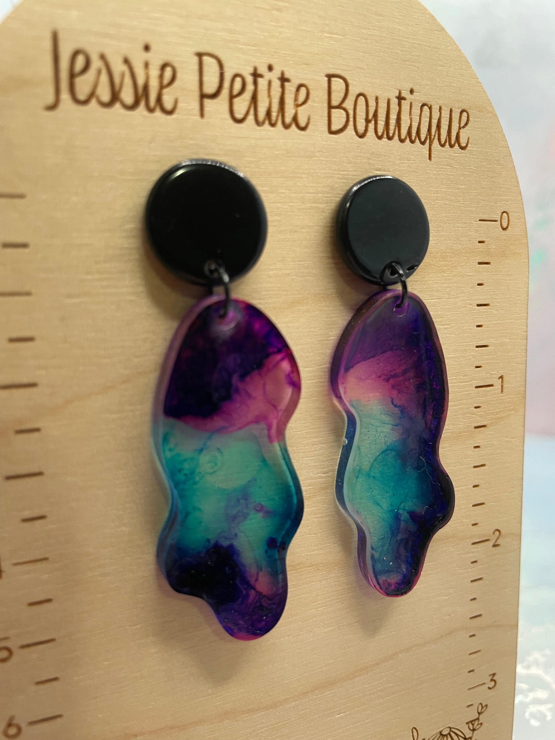 Colorful abstract earrings on a wooden surface with 'Jessie Petite Boutique' branding.