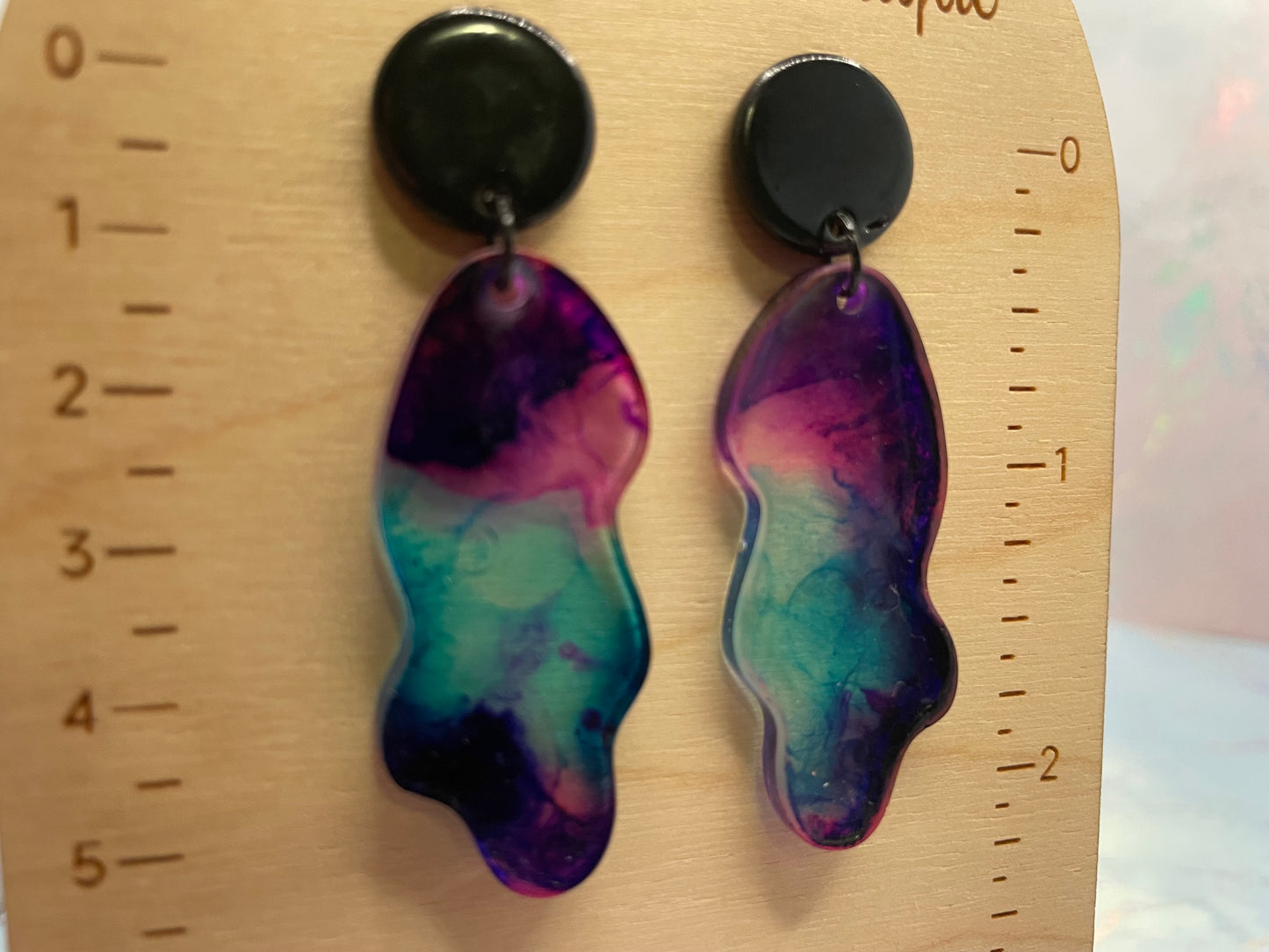 Pair of colorful earrings on a wooden ruler for scale.