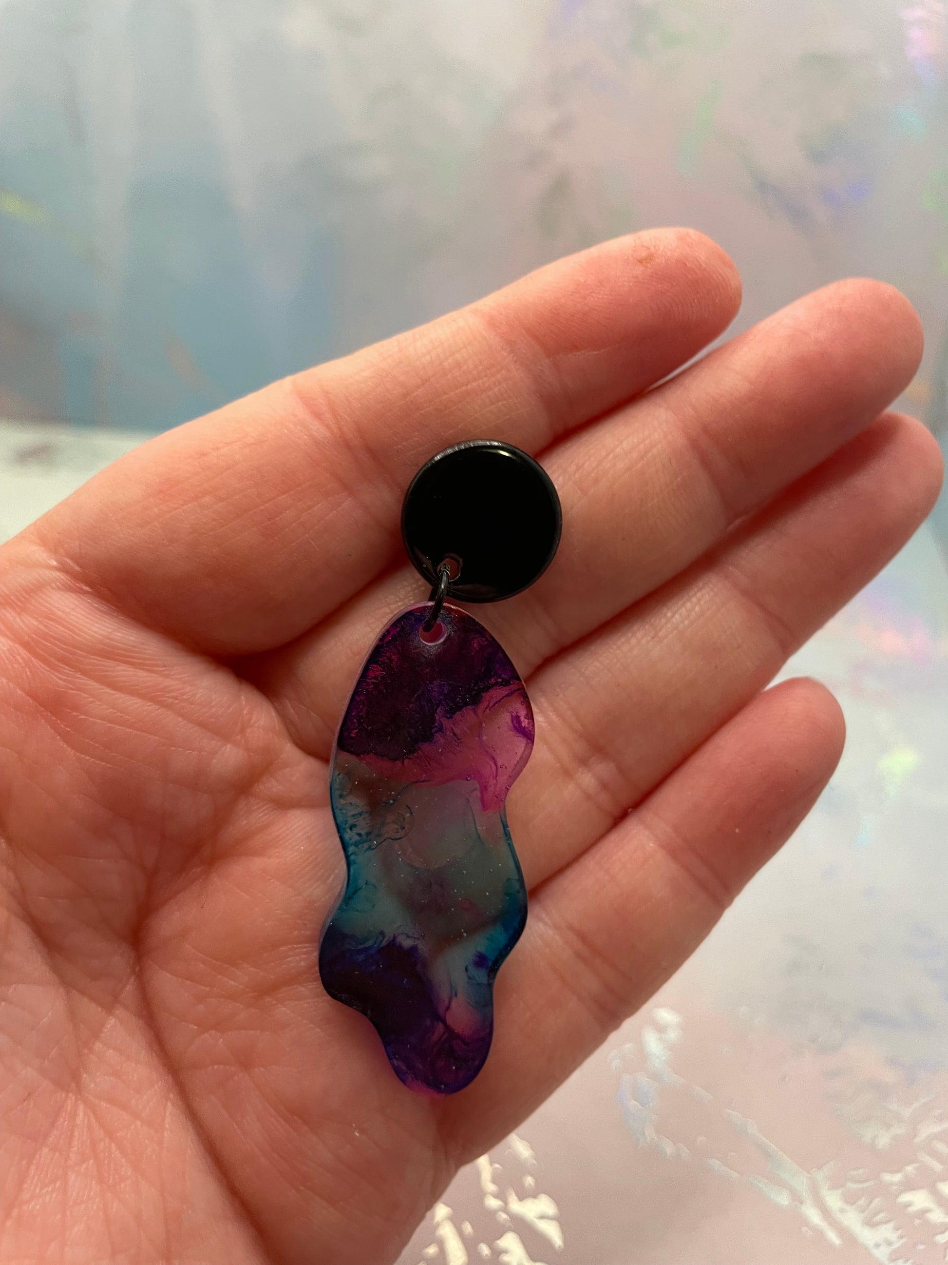 Hand holding a black and multicolored earring against a light background