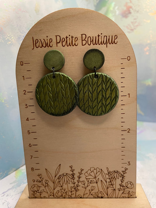 A pair of round knit earrings in green, displayed on a wooden stand with a brand name 'Jessie Petite Boutique'.