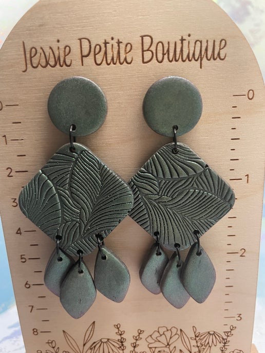 Green leaf-shaped earrings on a wooden card with 'Jessie Petite Boutique' branding.