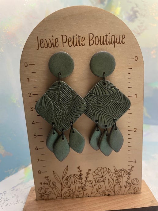 Green leaf-shaped earrings on a wooden display card with 'Jessie Petite Boutique' branding.