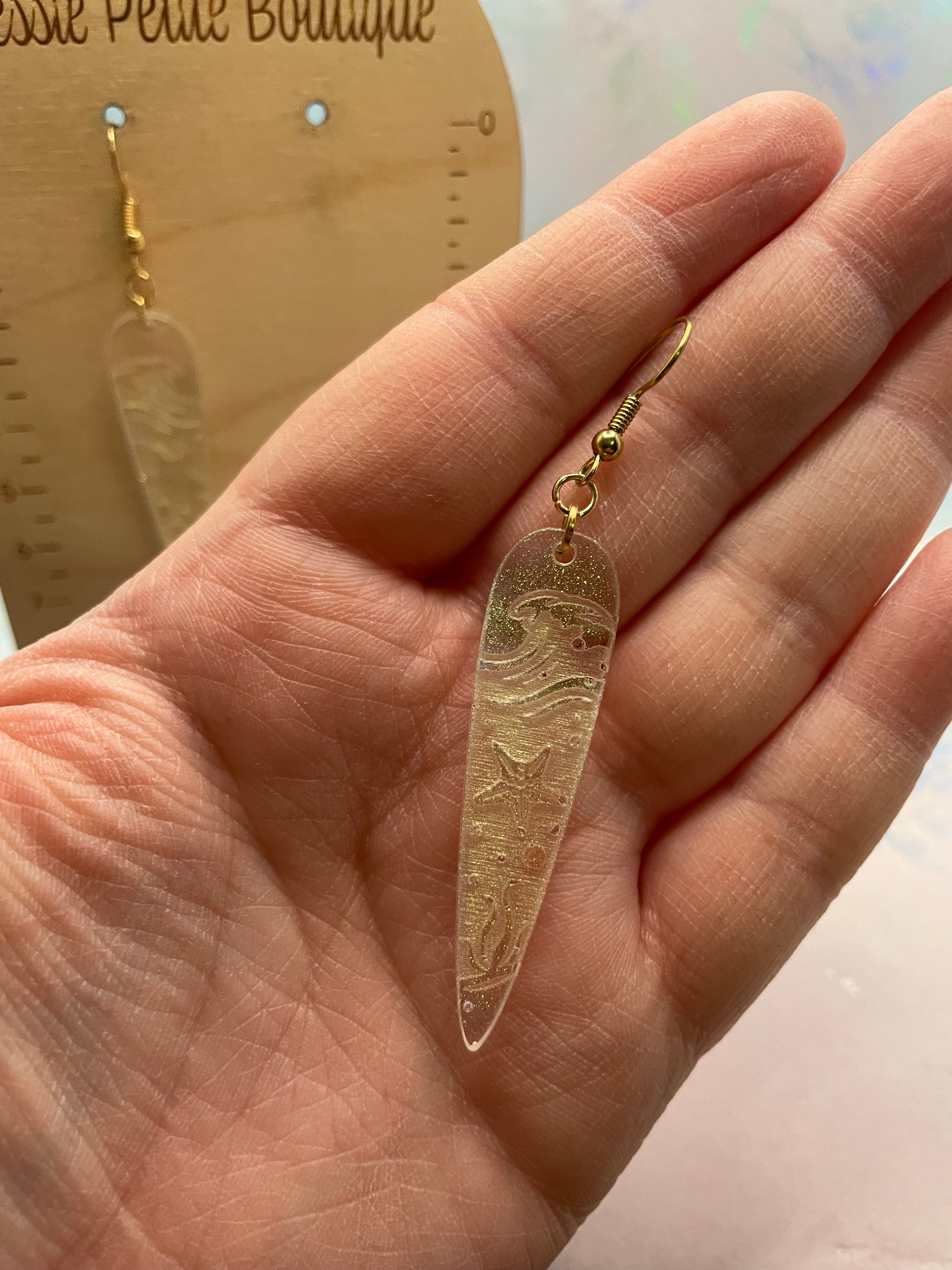 chameleon olive Ocean Wave Engraving: Earrings held in a hand with a blurred background