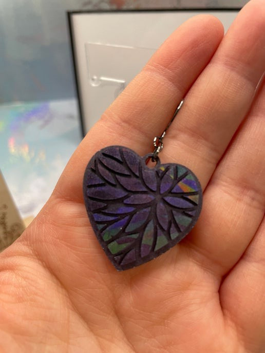 A pair of heart-shaped holographic dangle earrings in chameleon purple, displayed on a wooden stand with measurements.