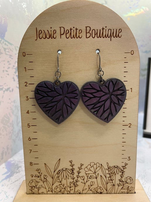A pair of heart-shaped holographic dangle earrings in chameleon purple, displayed on a wooden stand with measurements.