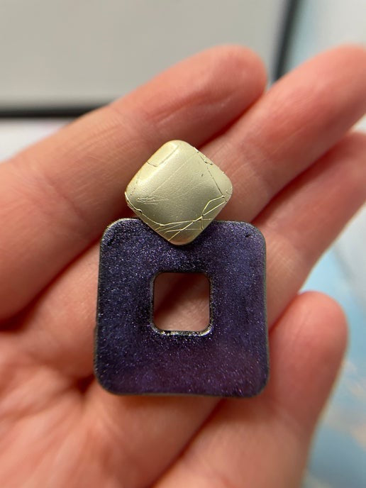 Purple square earring with gold top held between fingers