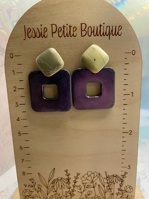 Pair of earrings on a wooden stand with 'Jessie Petite Boutique' branding.