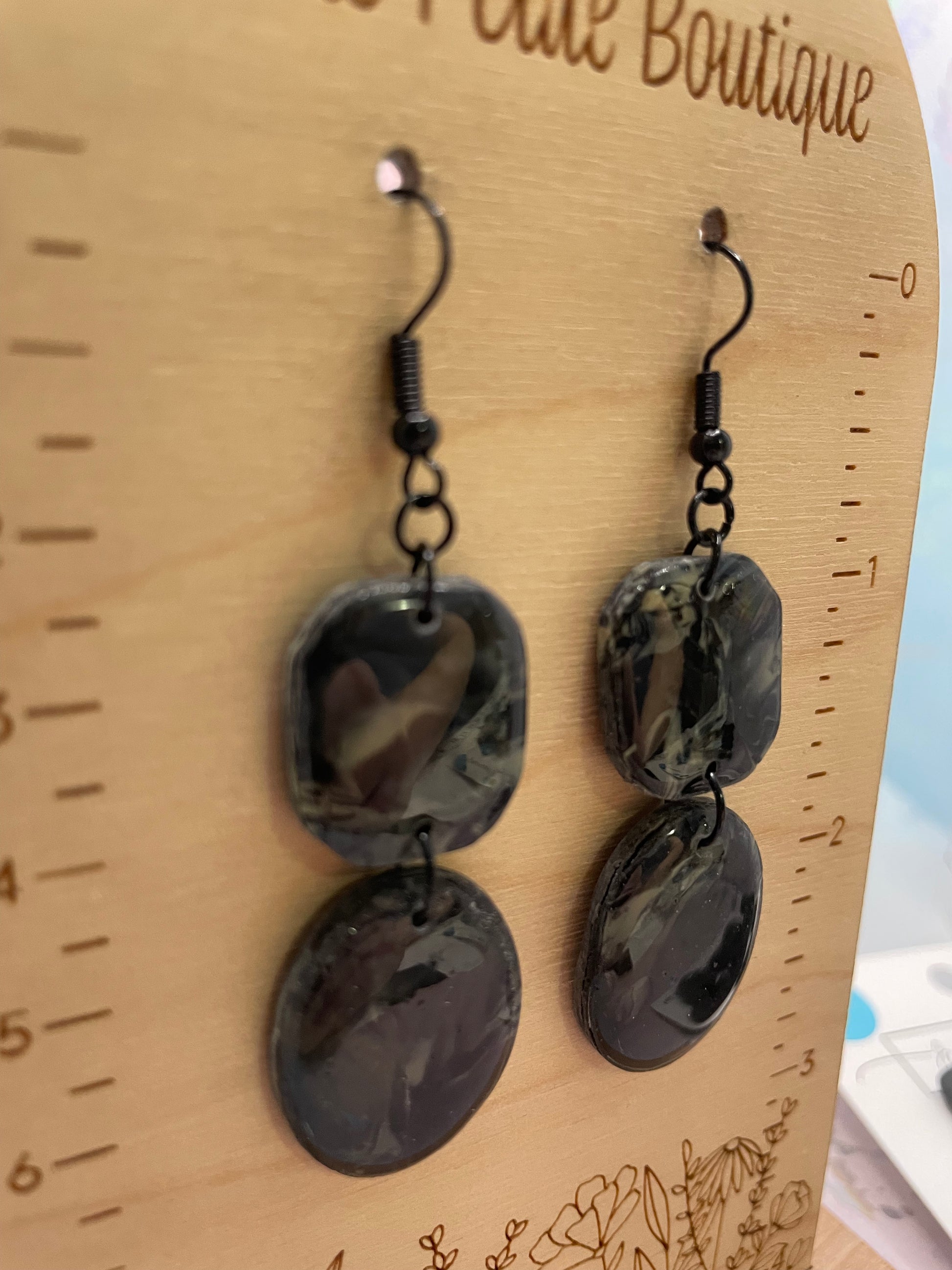 Pair of black marbled earrings on a wooden surface with a ruler for scale.