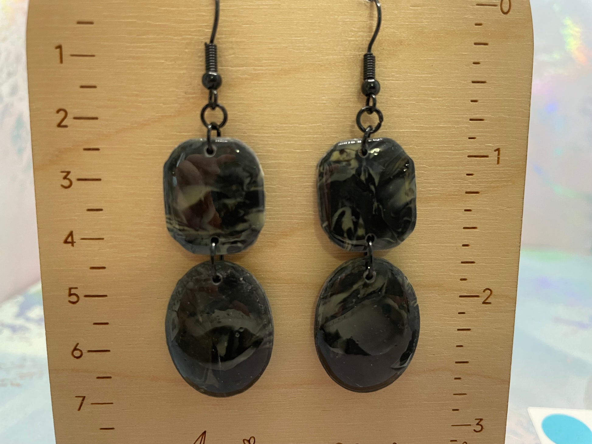 Pair of black marbled earrings on a wooden ruler for scale.