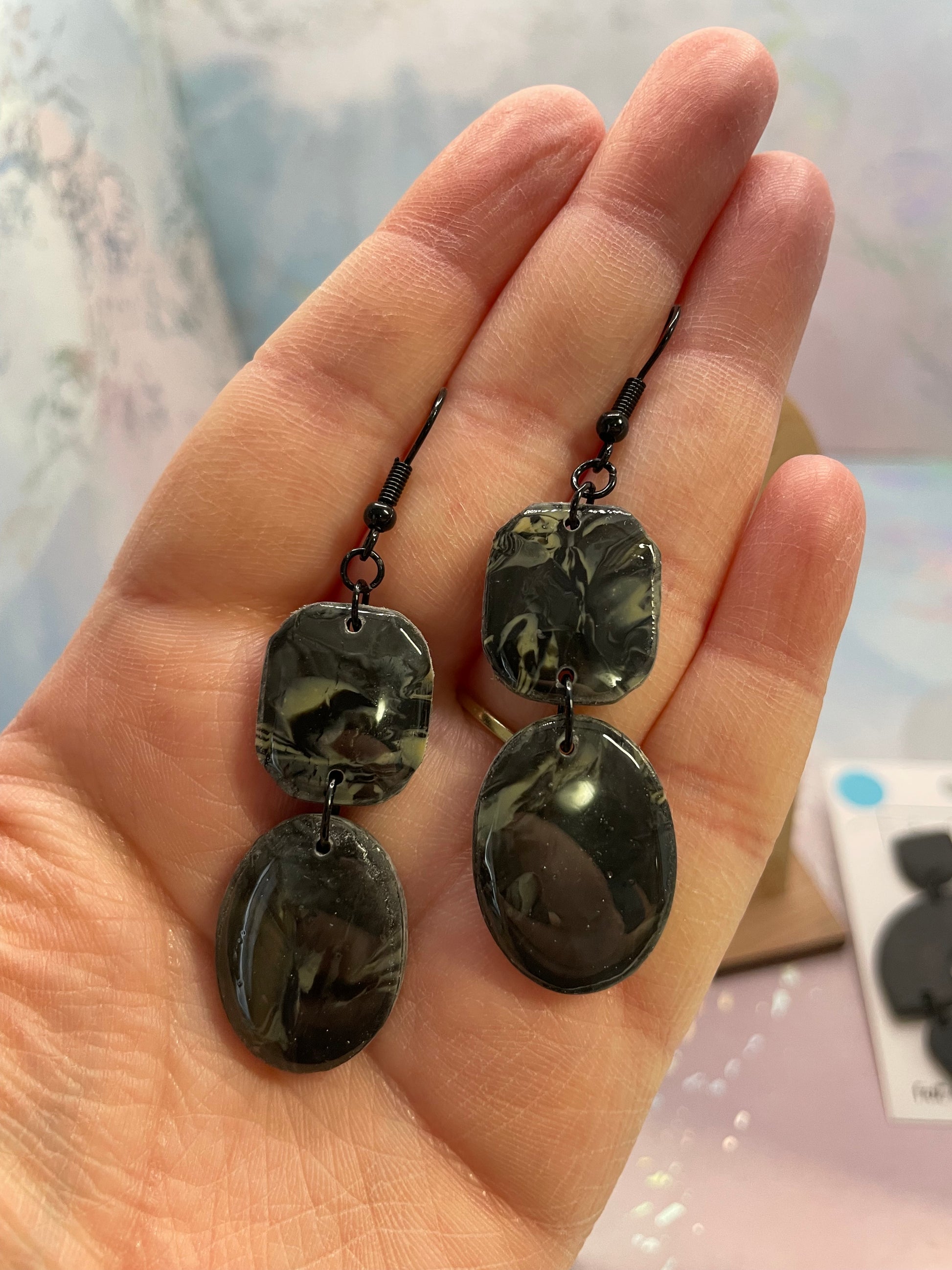 Hand holding a pair ofcharcoal black marbled: shayna earrings with a blurred background