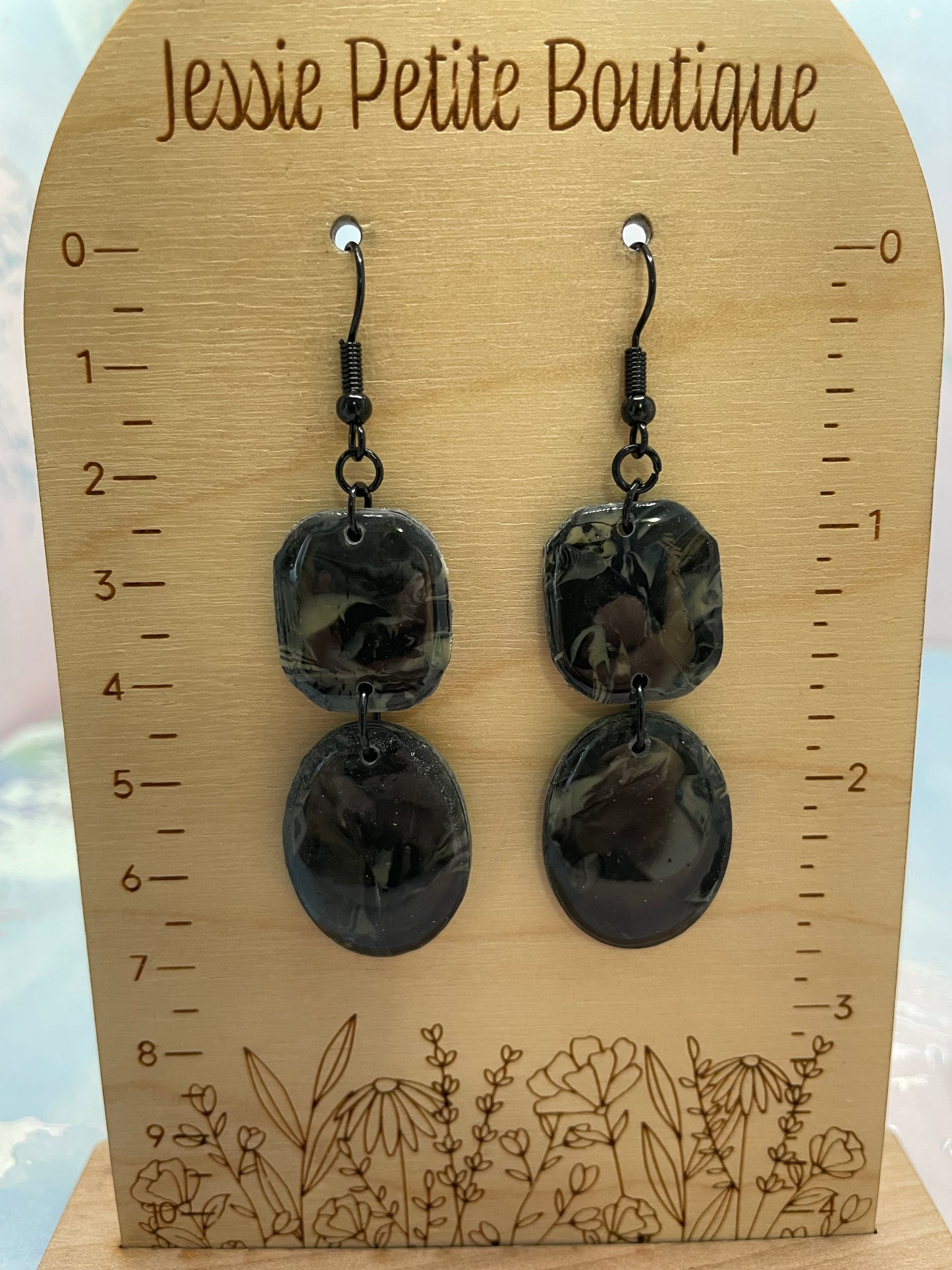 Pair of black earrings on a wooden card with measurements and floral design.