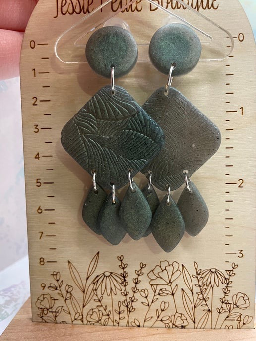 Green earrings on a wooden display card with floral designs