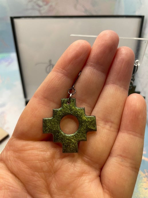 Hand holding a green cross-shaped pendant with a blurred background