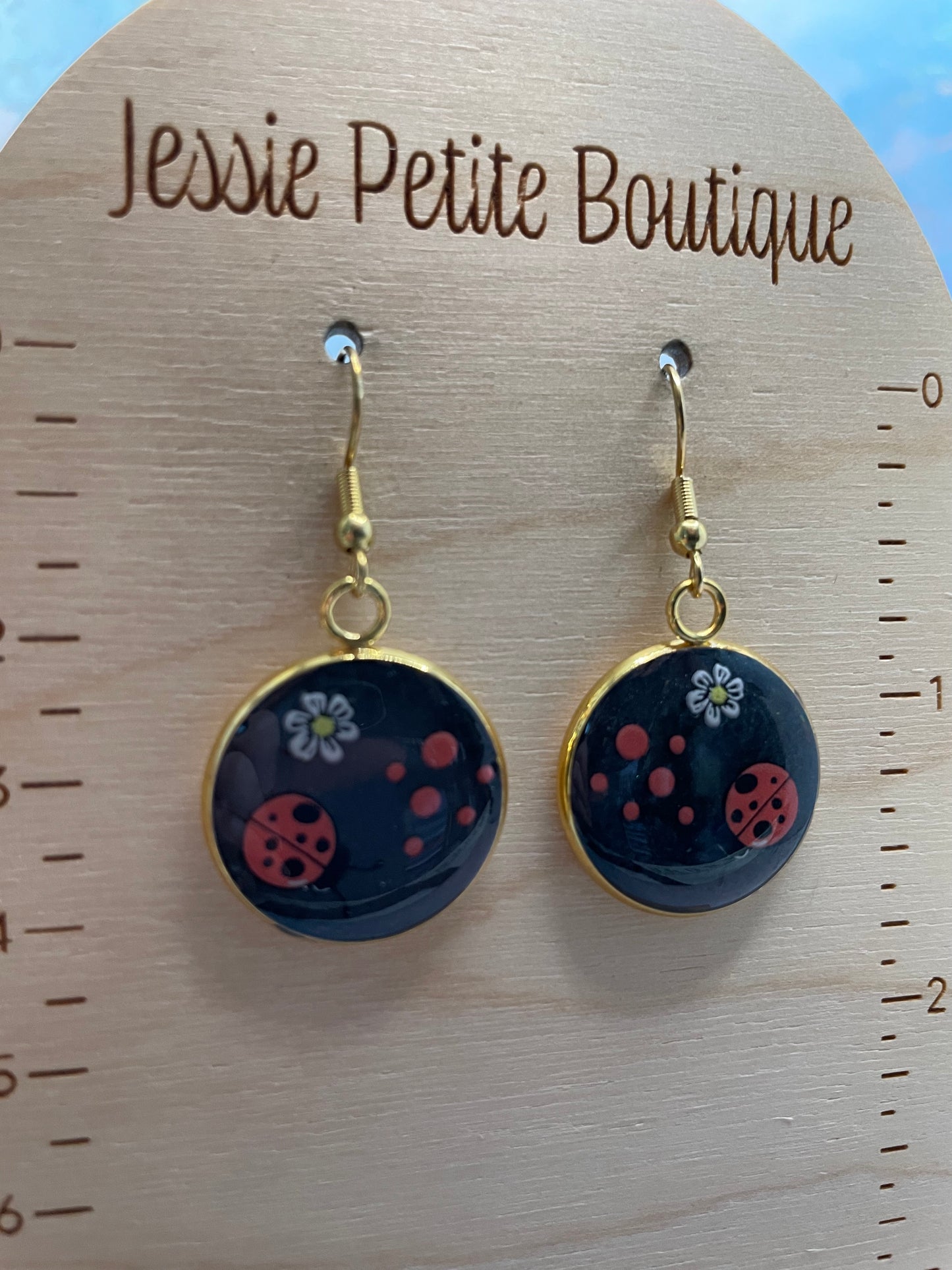 Pair of earrings with floral design on a wooden display card with measurement scale and 'JessiePetite Boutique' branding.