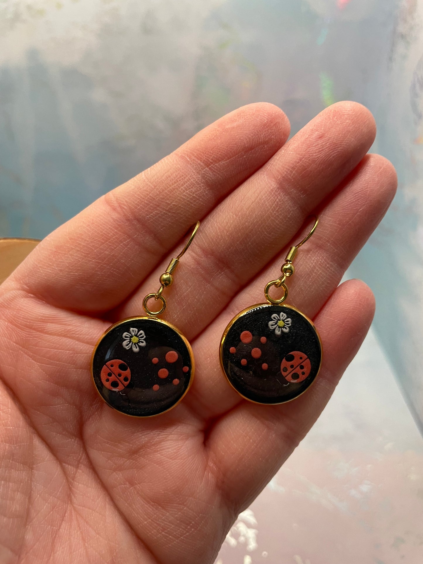 Hand holding a pair of earrings with black and gold designs.