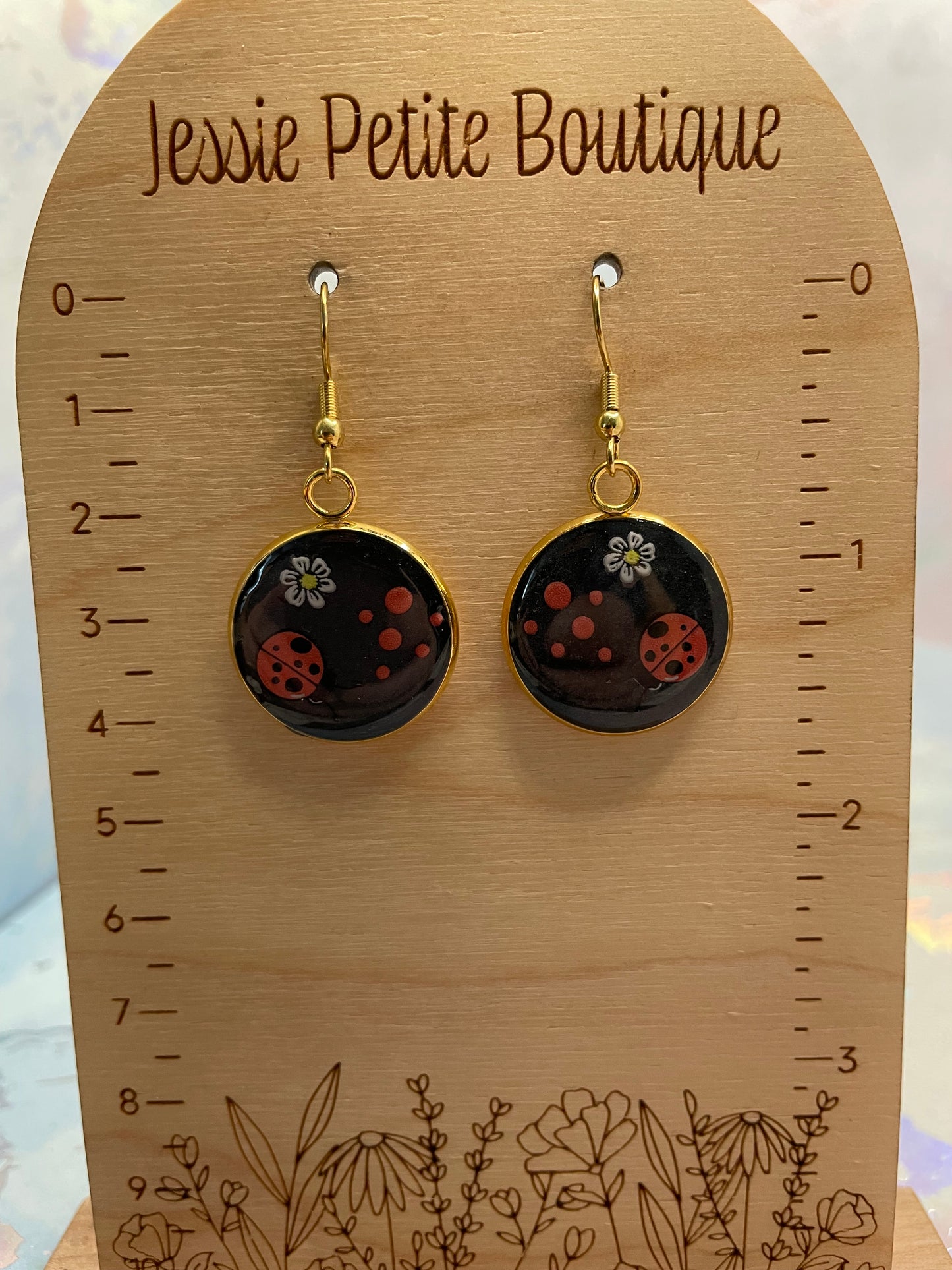 Pair of earrings on a wooden display card with measurements and floral designs.