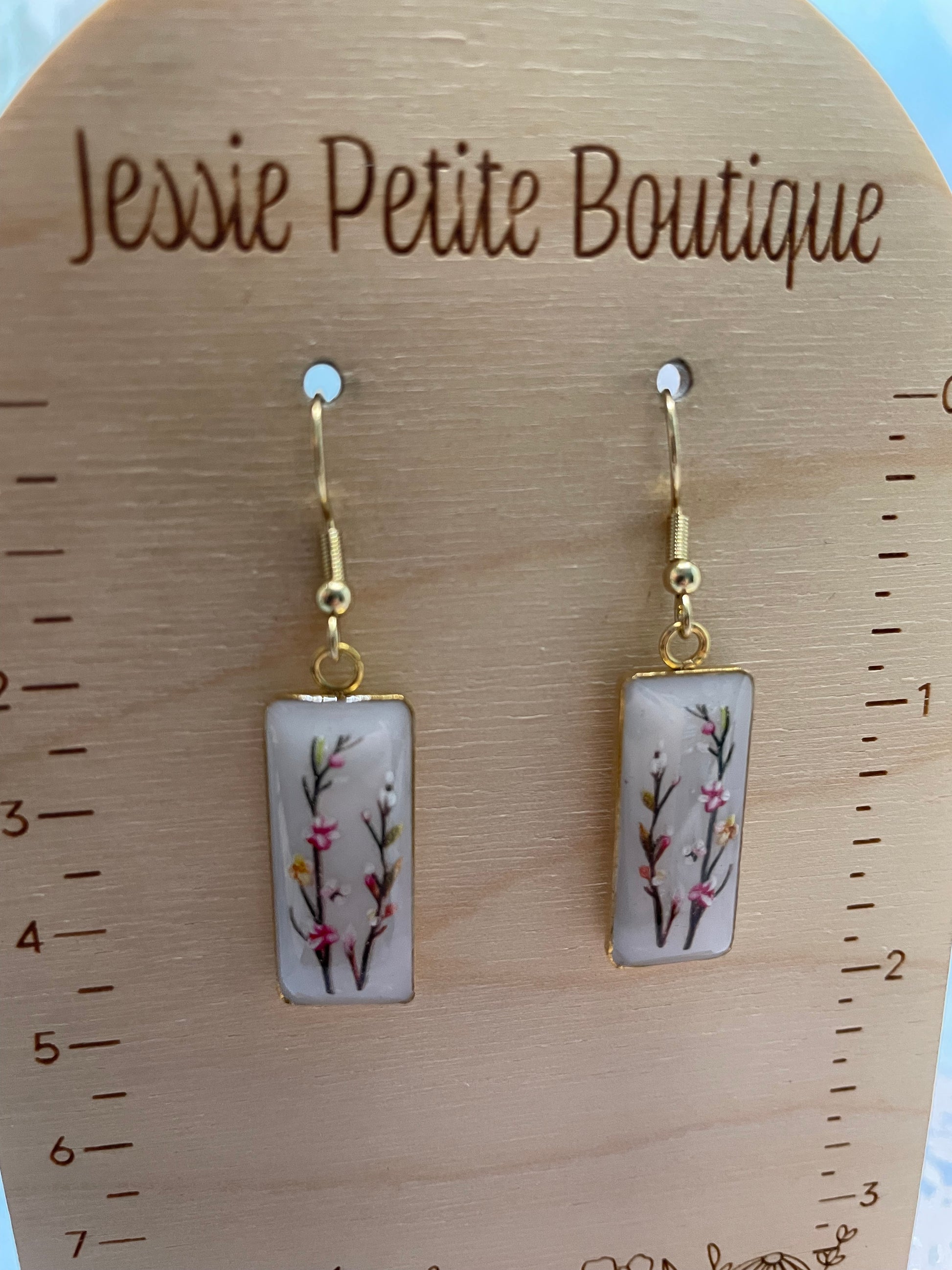Pair of earrings with floral design on a wooden display card with 'Jessie Petite Boutique' branding.
