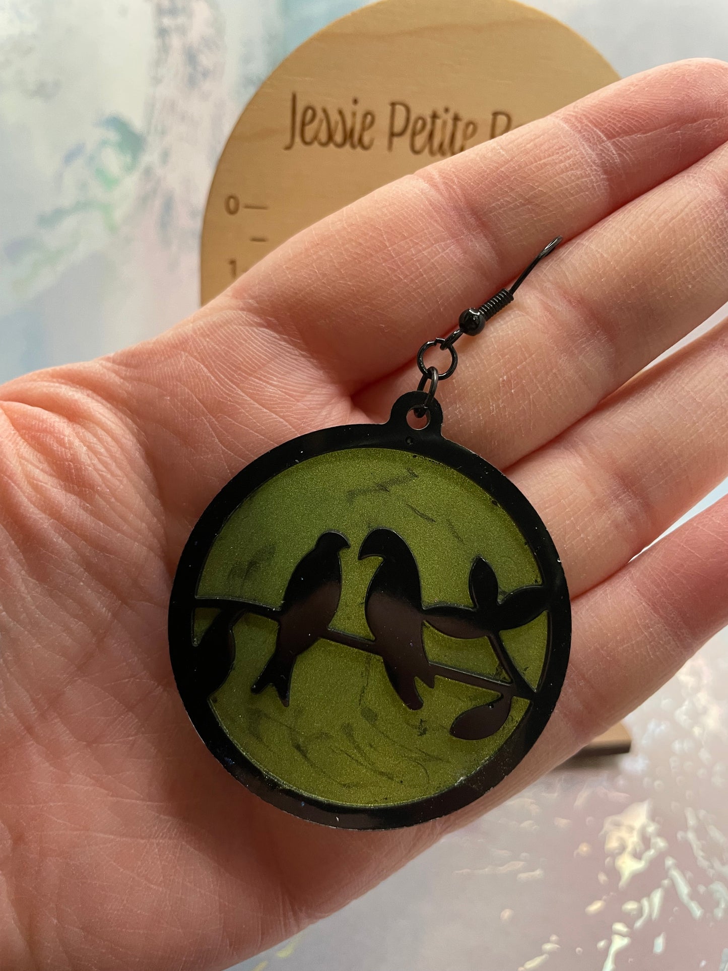 Hand holding a round pendant with a bird design on a light background