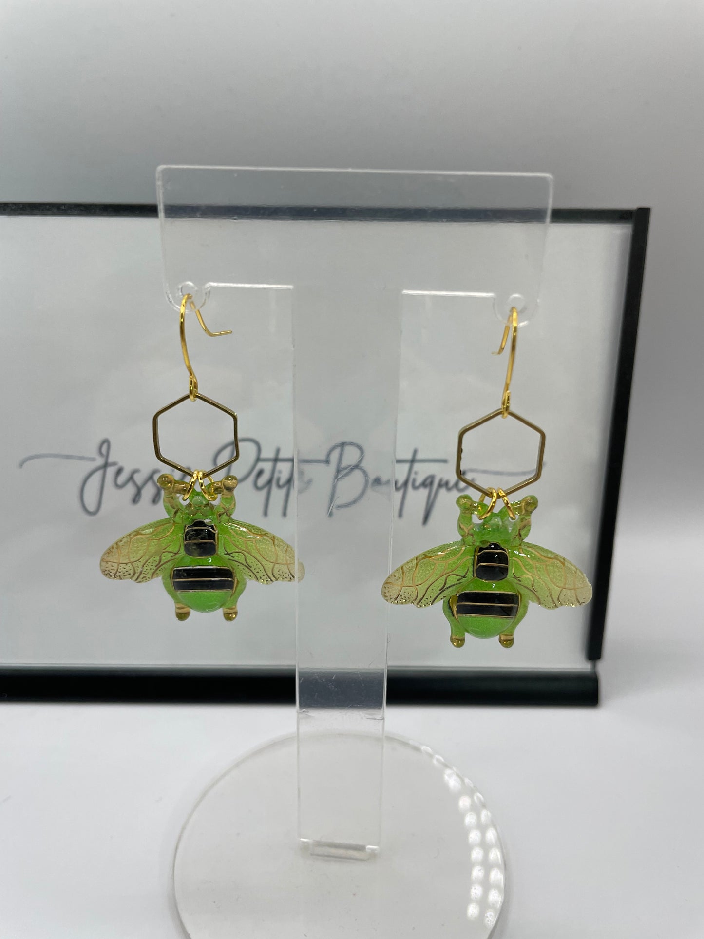 Green insect-shaped earrings on a clear stand with a white background