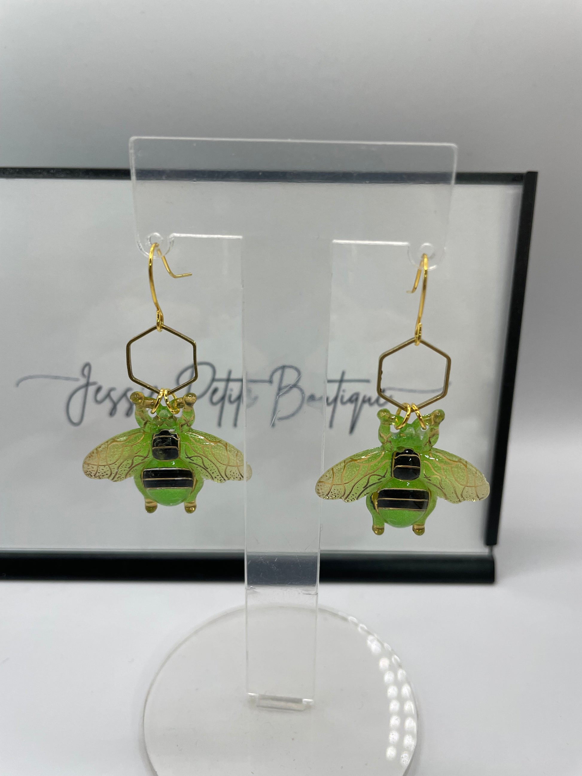Green insect-shaped earrings on a clear stand with a white background
