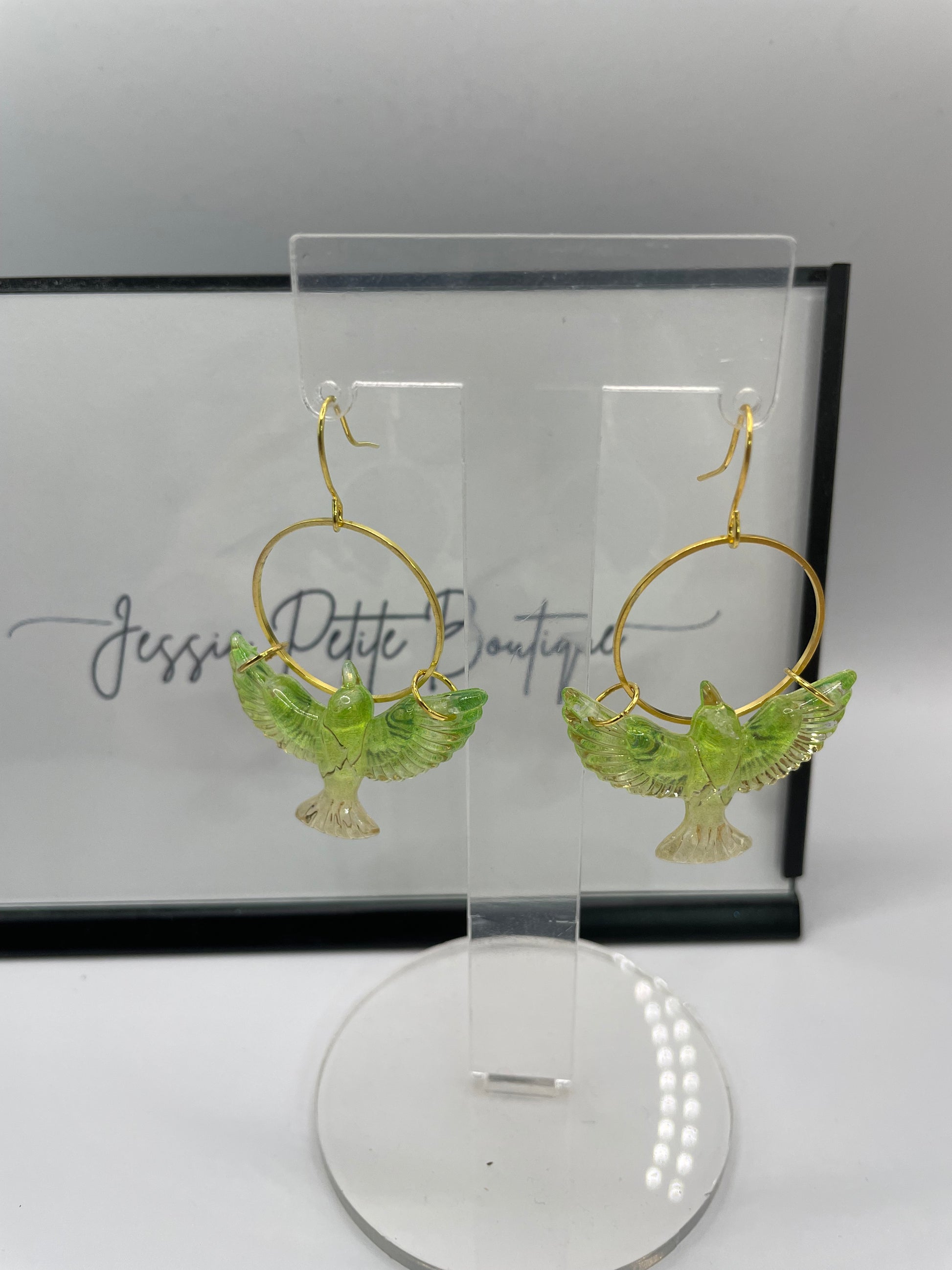 Green bird-shaped earrings in a clear display case with a light source.