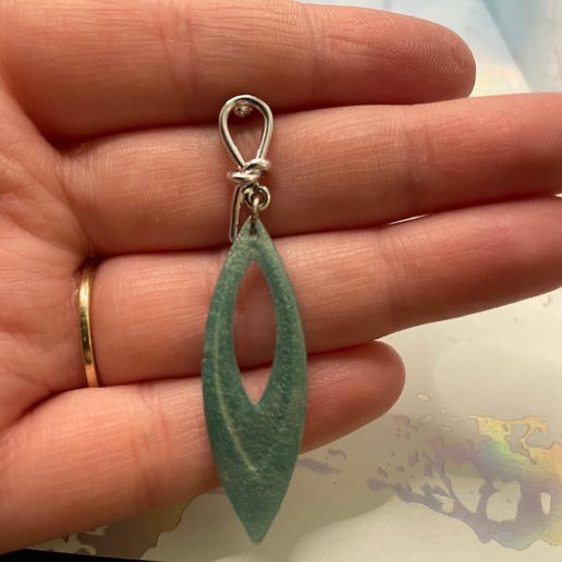 Green teardrop-shaped pendant on a silver lasso held in a hand.