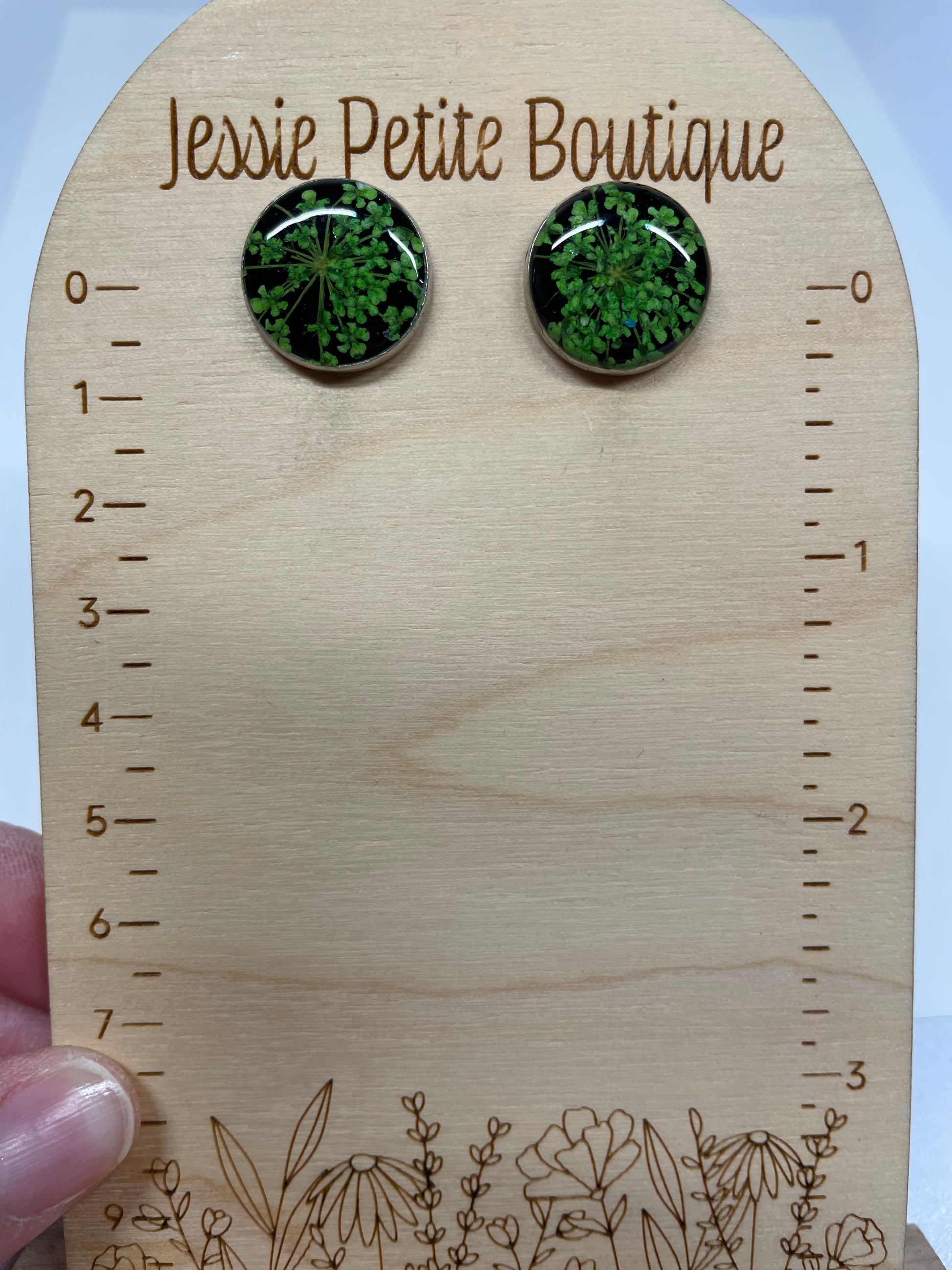 Pair of green earrings on a wooden card with floral designs and measurements.