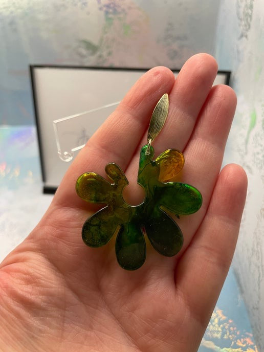 Hand holding a green glass flower-shaped object against a blurred background