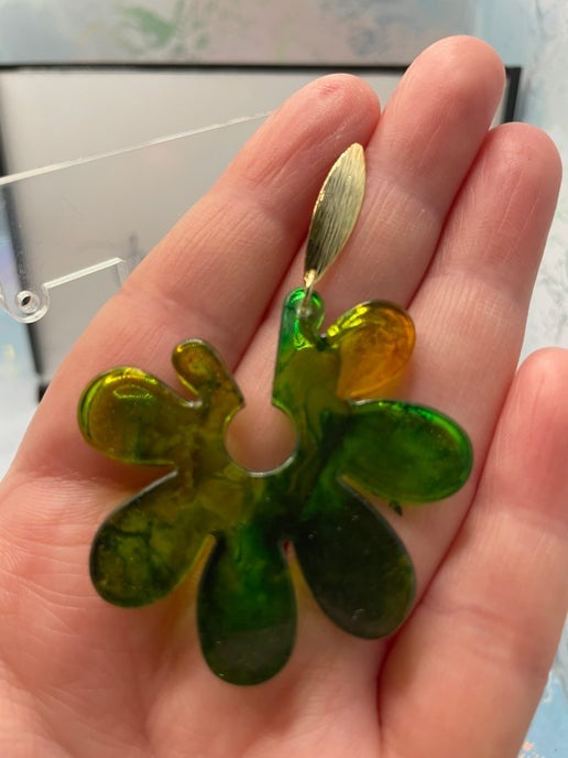 Green and gold four-leaf clover-shaped earring held in a hand.