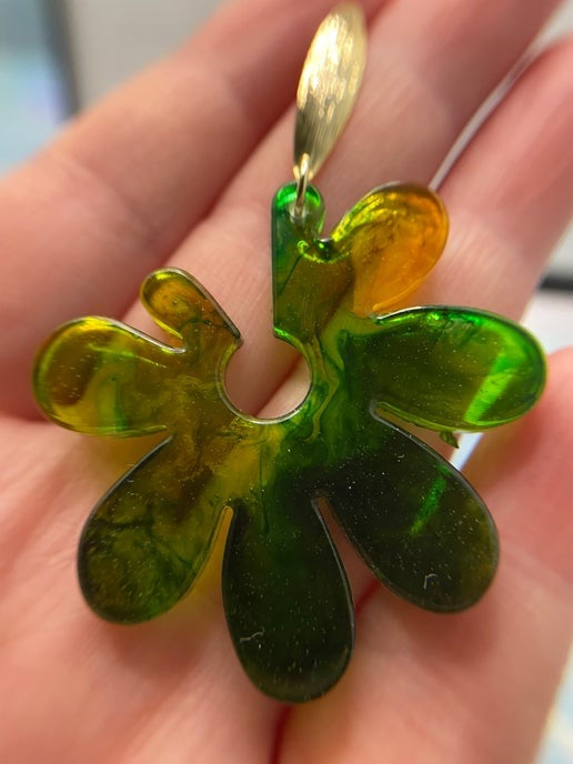 Green and orange floral-shaped earring held between fingers