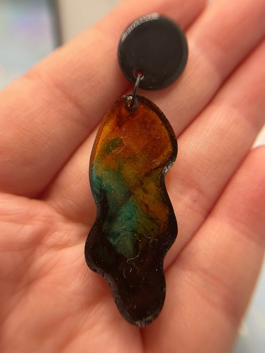 Multicolored earring held in a hand with a blurred background