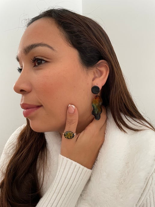 Woman wearing colorful earrings and a white sweater against a plain background