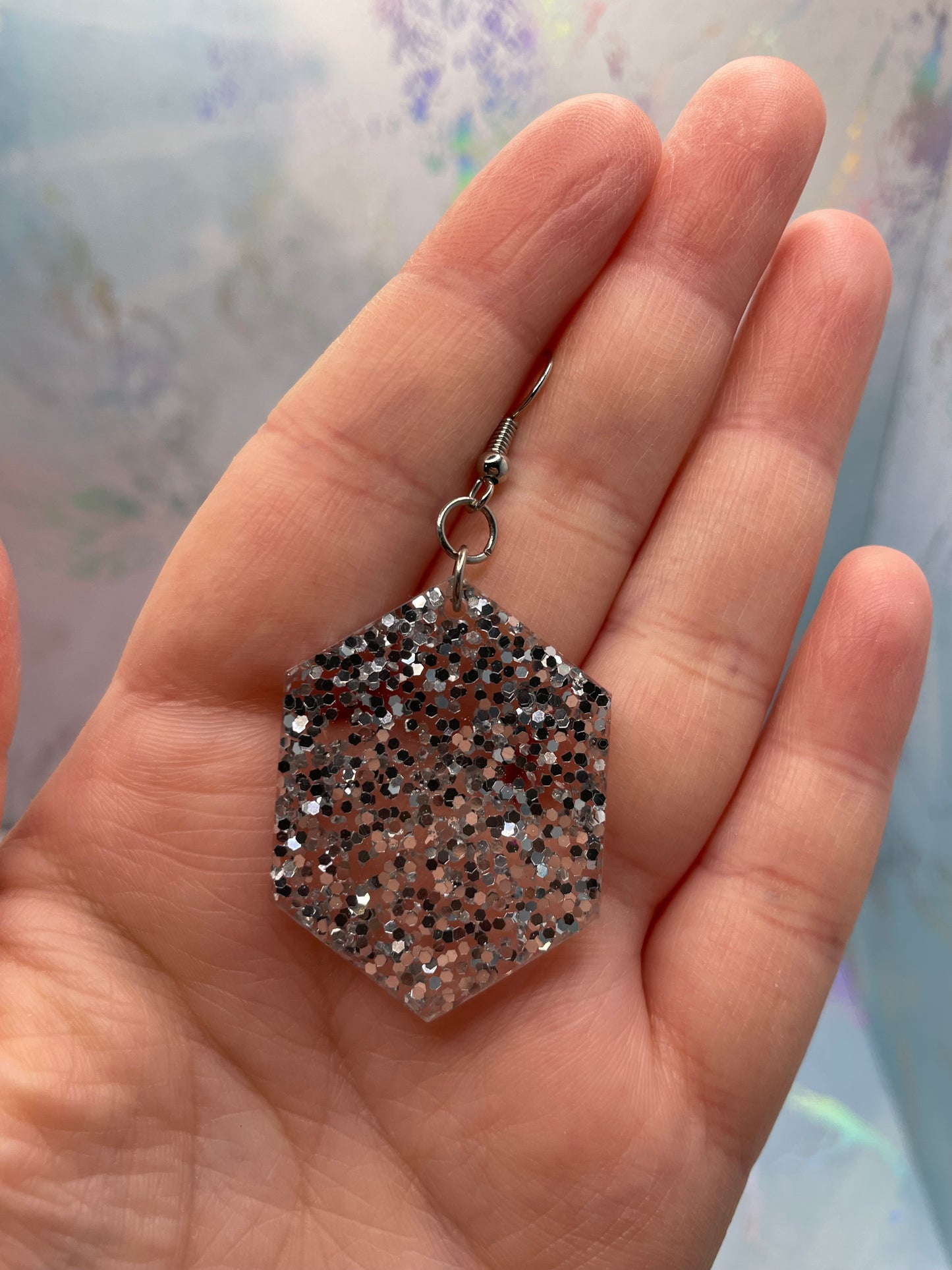 Hexagonal glittery earring held in a hand with a blurred background