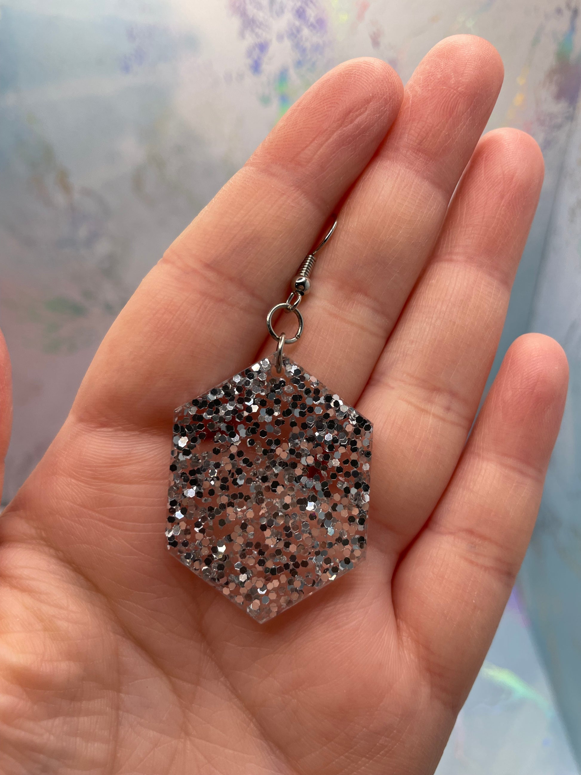 Hexagonal glittery earring held in a hand with a blurred background