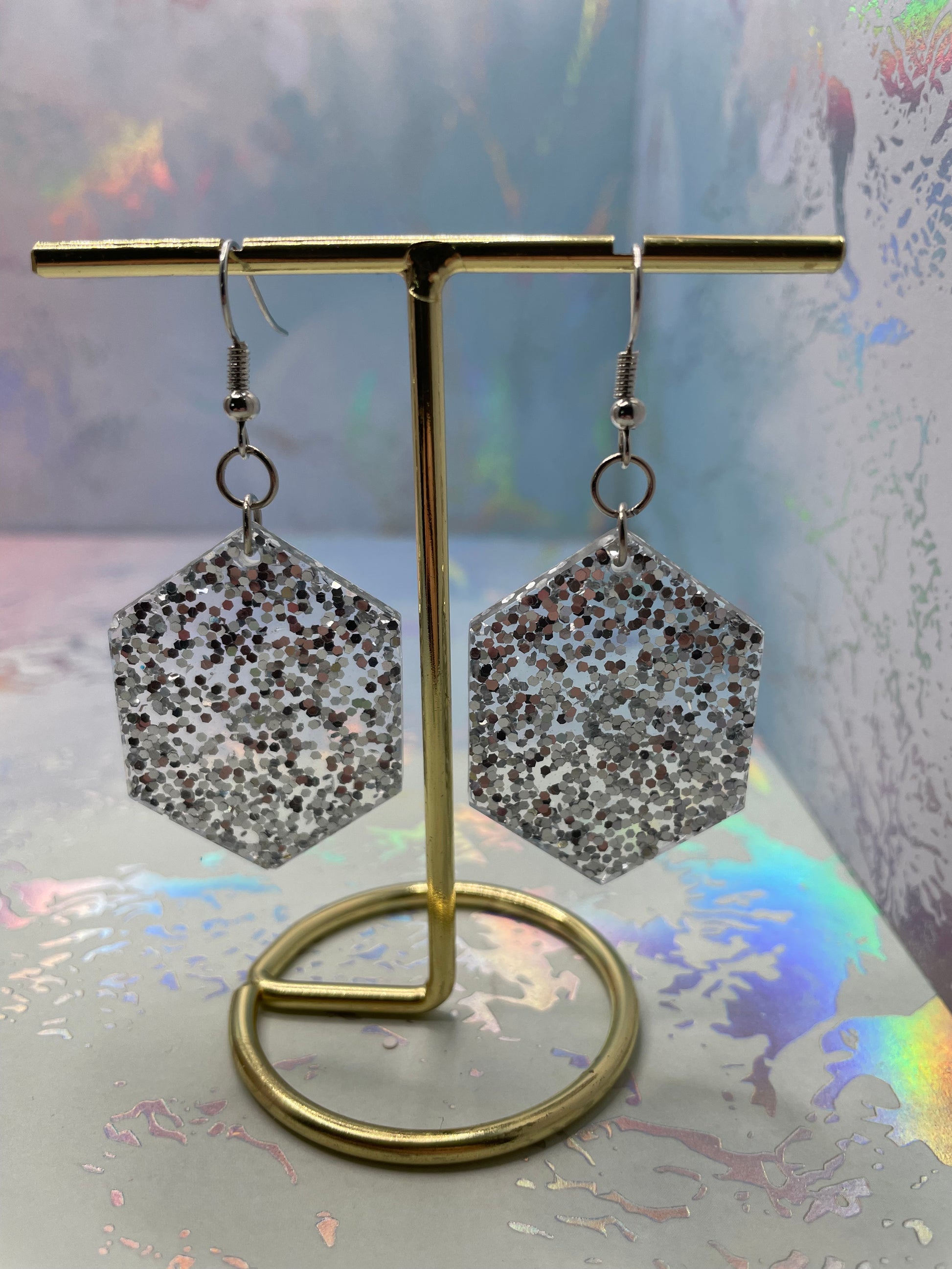 Hexagonal earrings on a stand with a colorful, abstract background