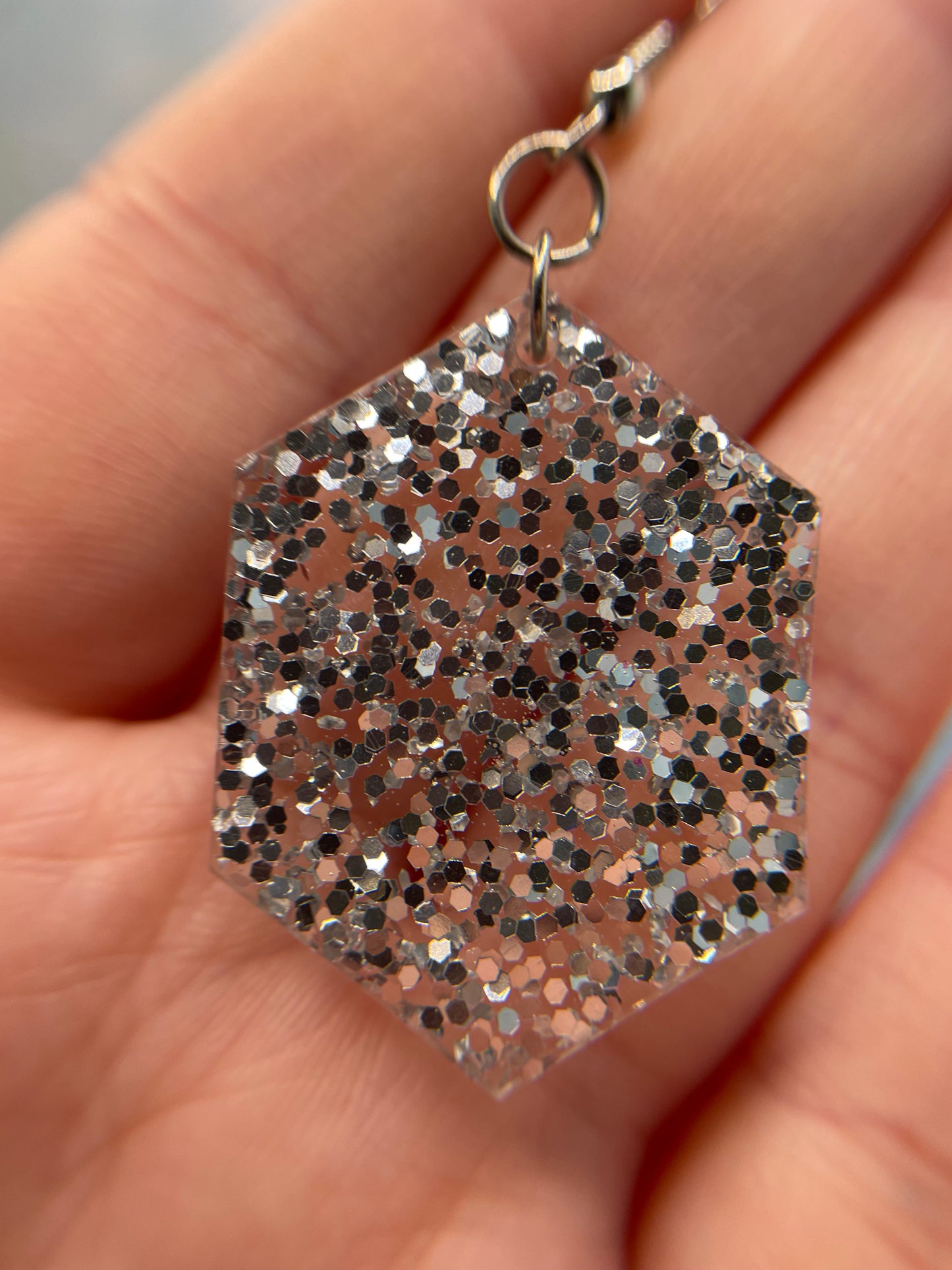 Hexagonal glittery earring held in a hand