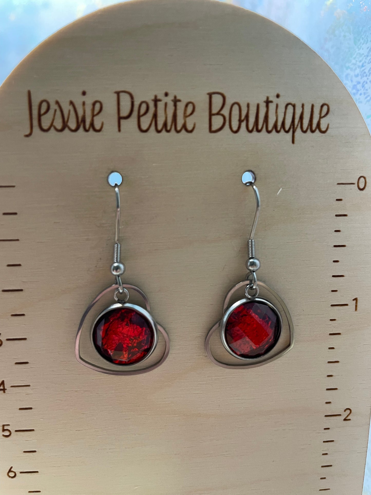 Red earrings on a wooden stand with 'Jessie Petite Boutique' branding.
