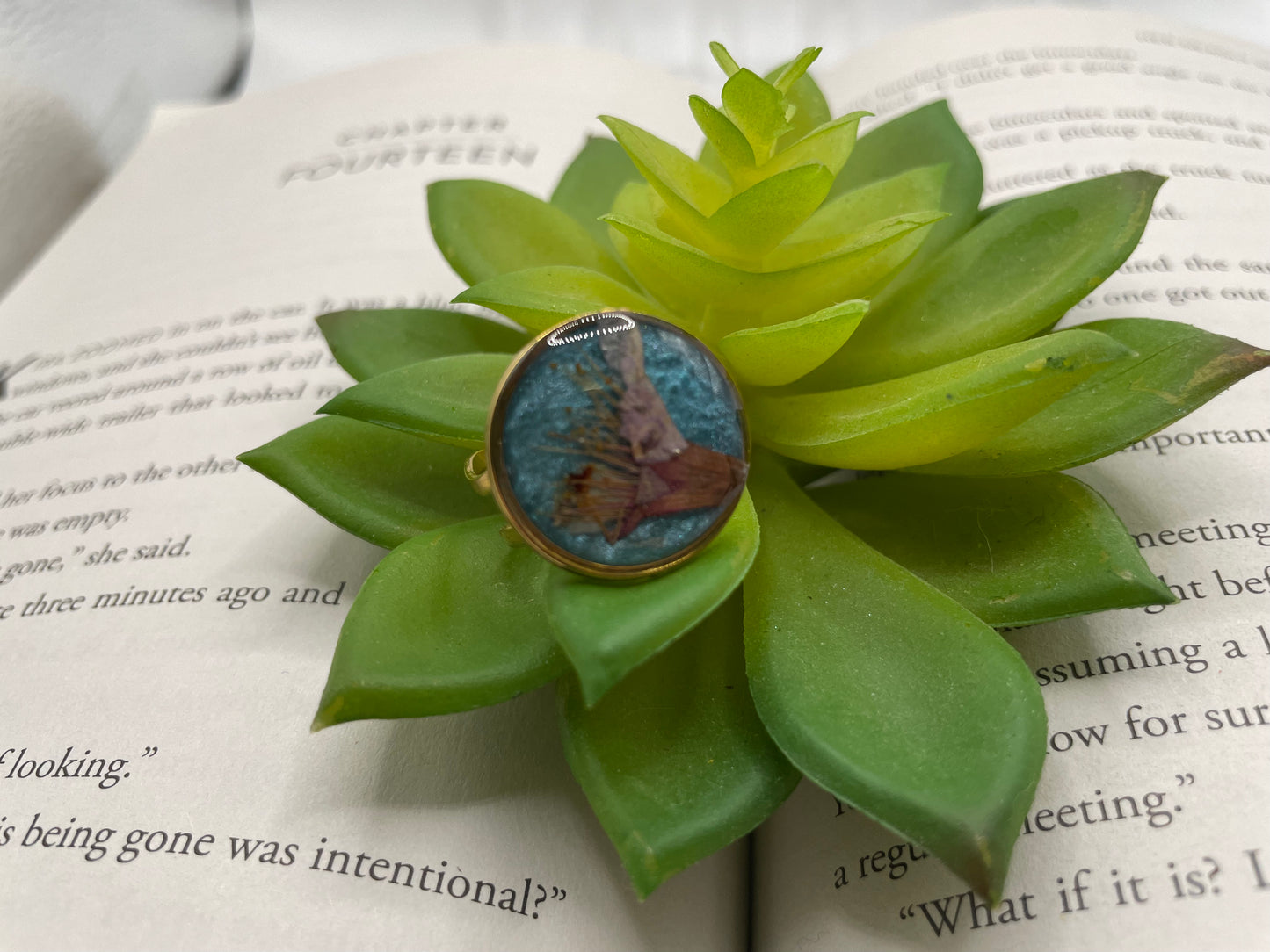 Ring with a blue hydrangea flower on a green succulent leaf on an open book