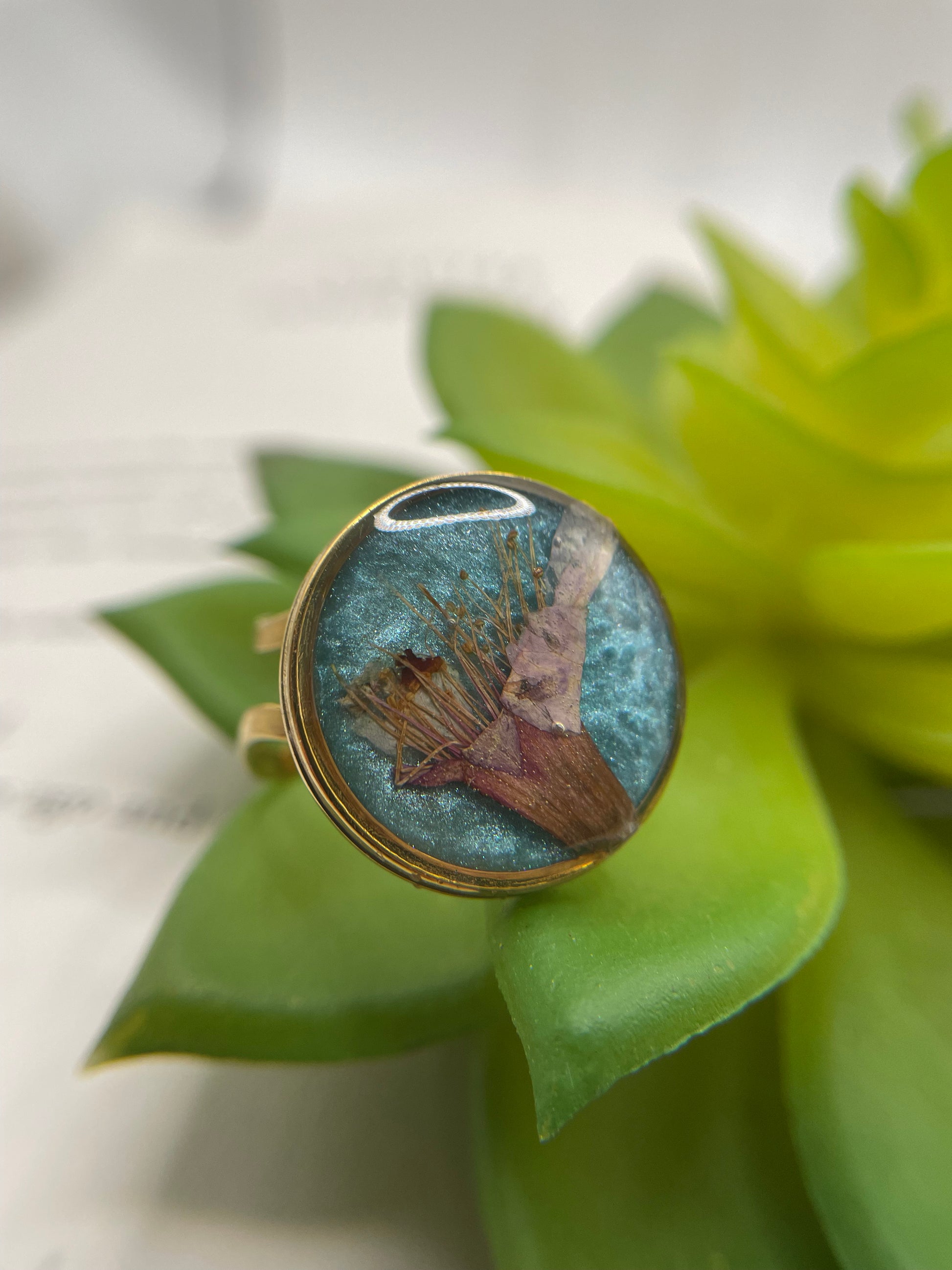 Ring with a blue stone and gold band on green leaves