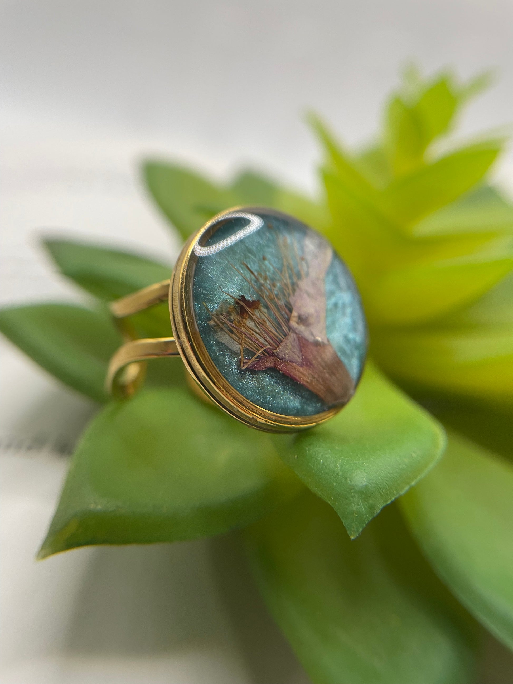 Gold ring with a nature-themed stone on green leaves