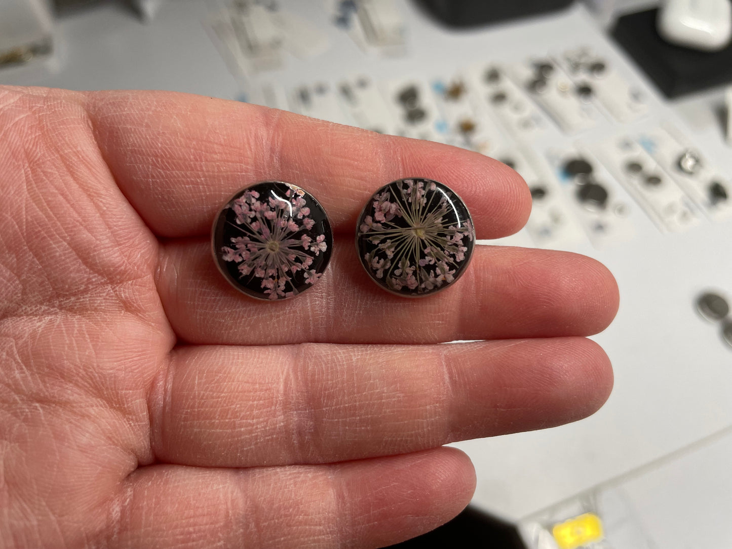 Pair of floral stud earrings held between fingers with a blurred background