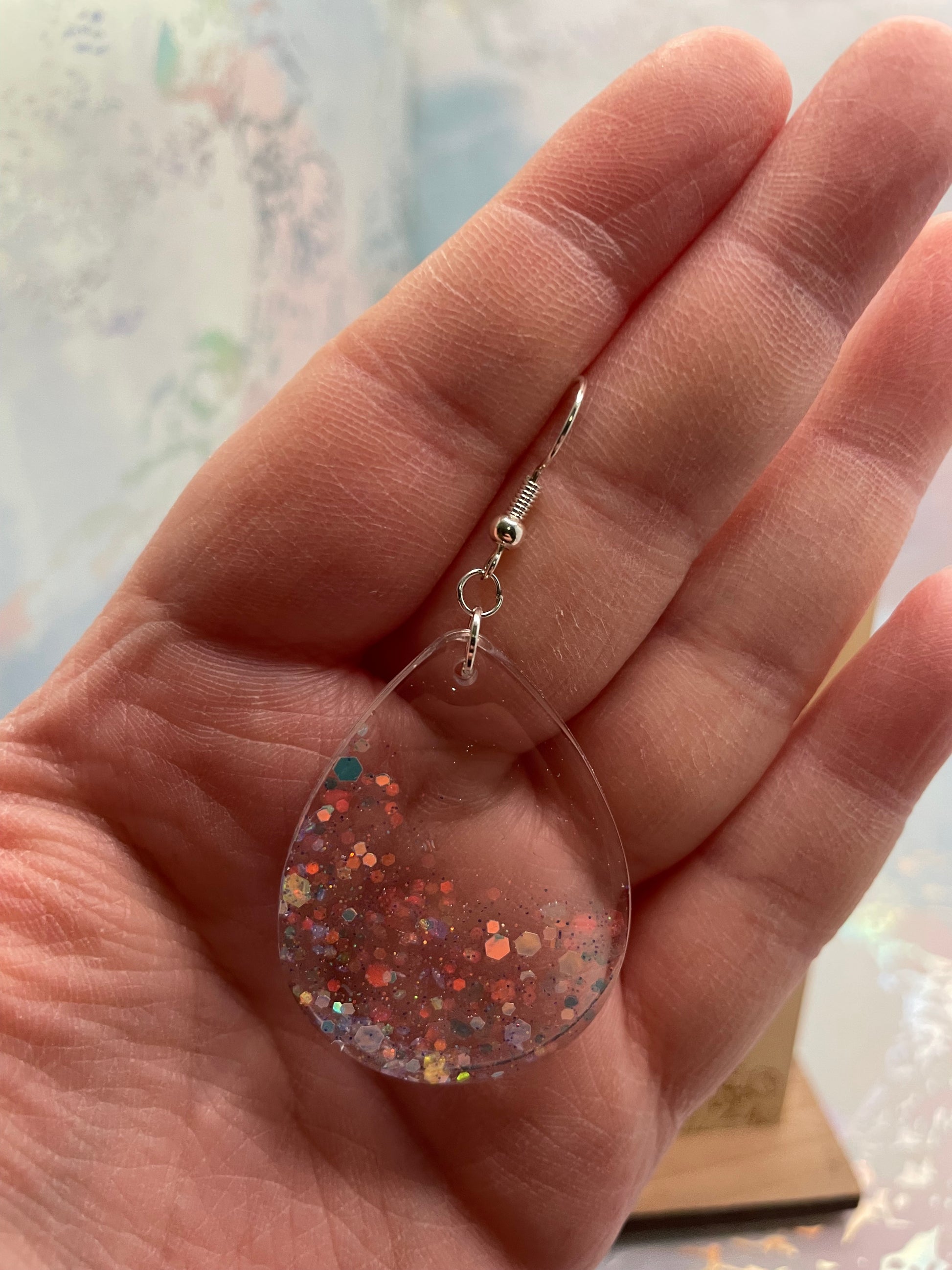 Hand holding a clear earring with glittery design against a blurred background
