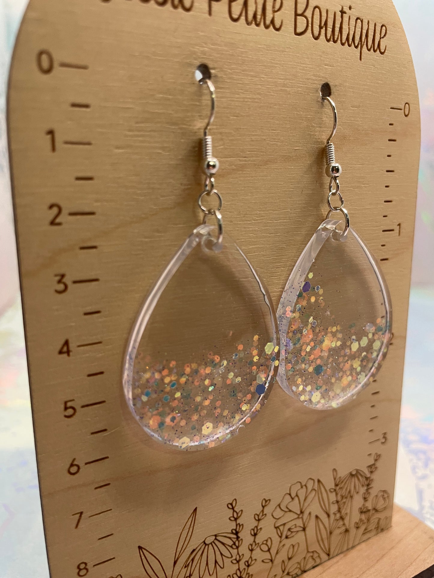 medium-sparkly teardrop earrings on a wooden scale with 'Jessie Petite Boutique' branding.
