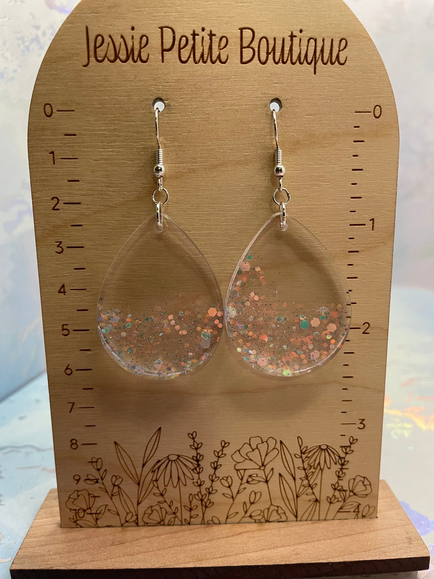 medium-sparkly teardrop earrings on a wooden display card with measurement scale and floral design.