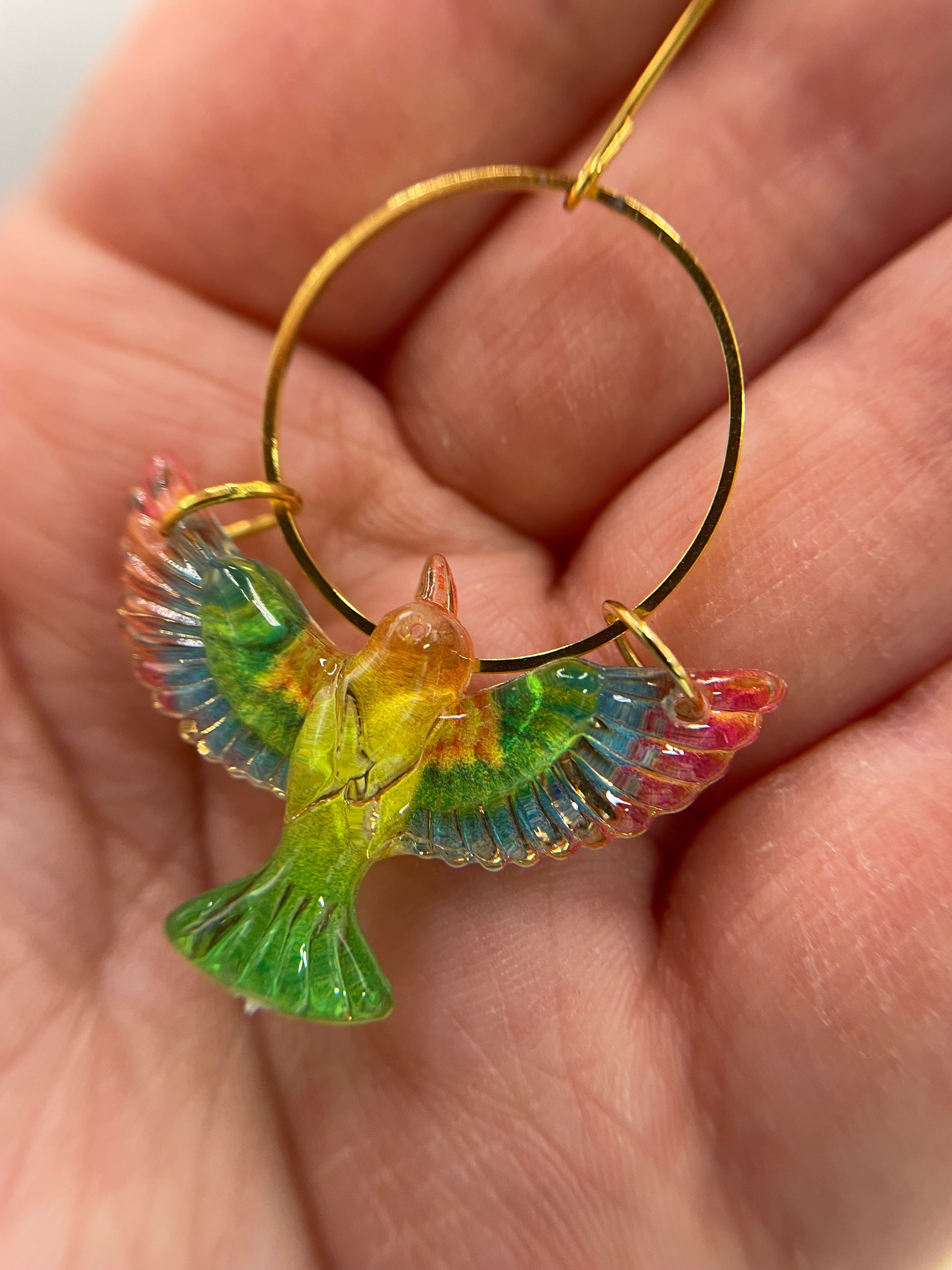 Colorful bird-shaped earring held in a hand