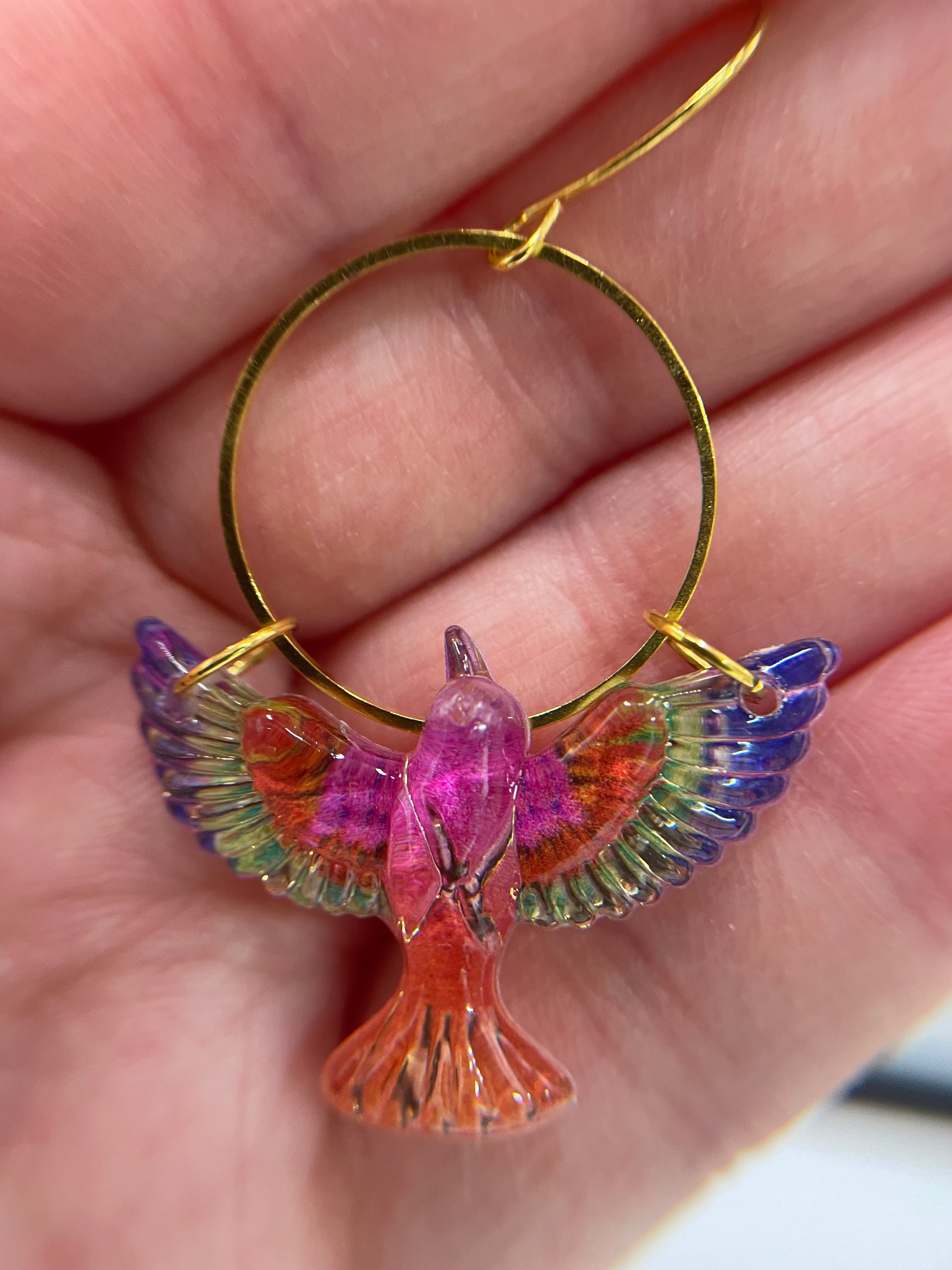 Colorful bird-shaped earring held in a hand