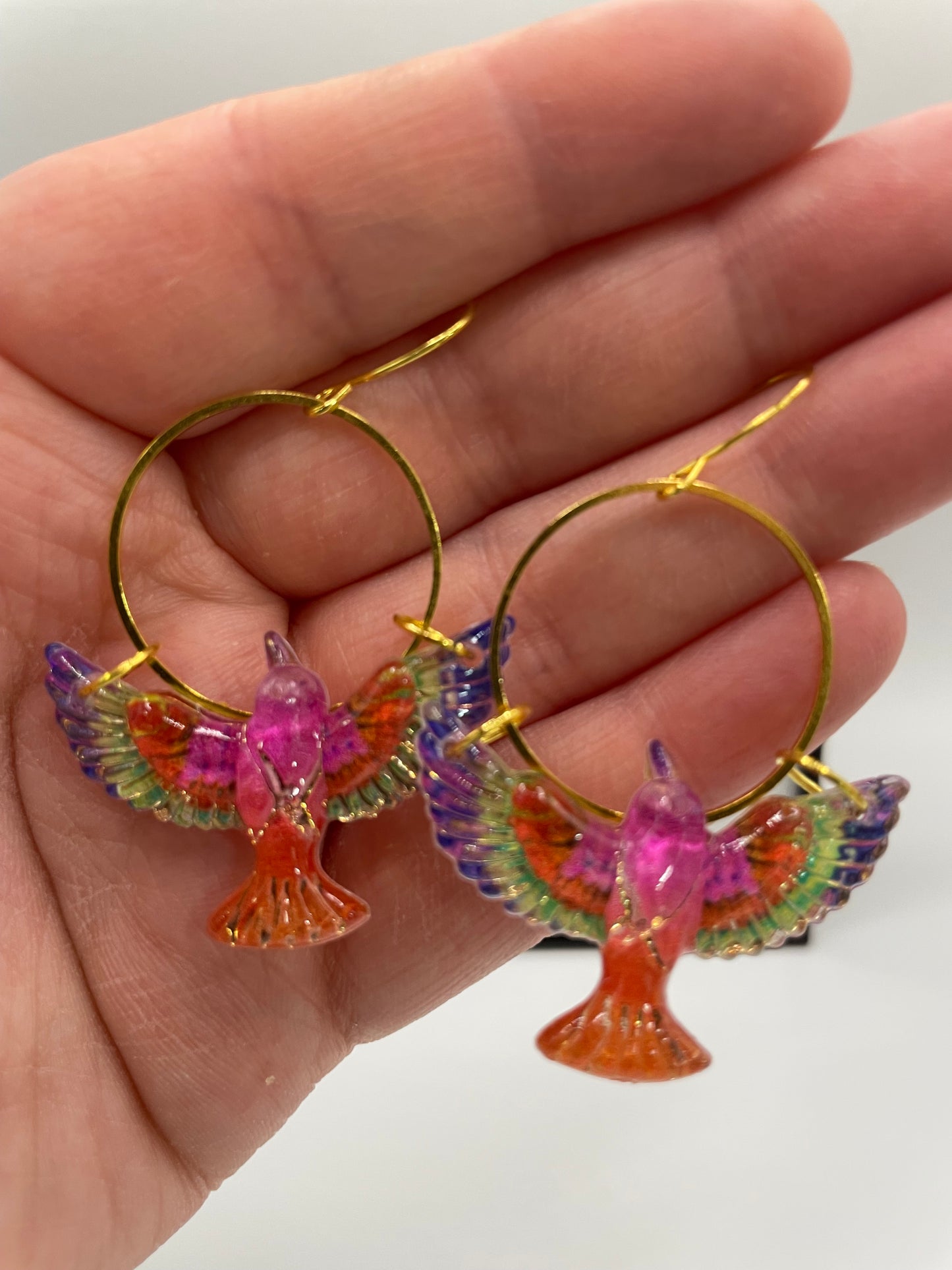 Colorful bird-shaped earrings held in a hand against a white background