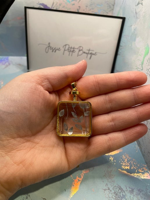 Hand holding a square-shaped pendant with floral design against a blurred background